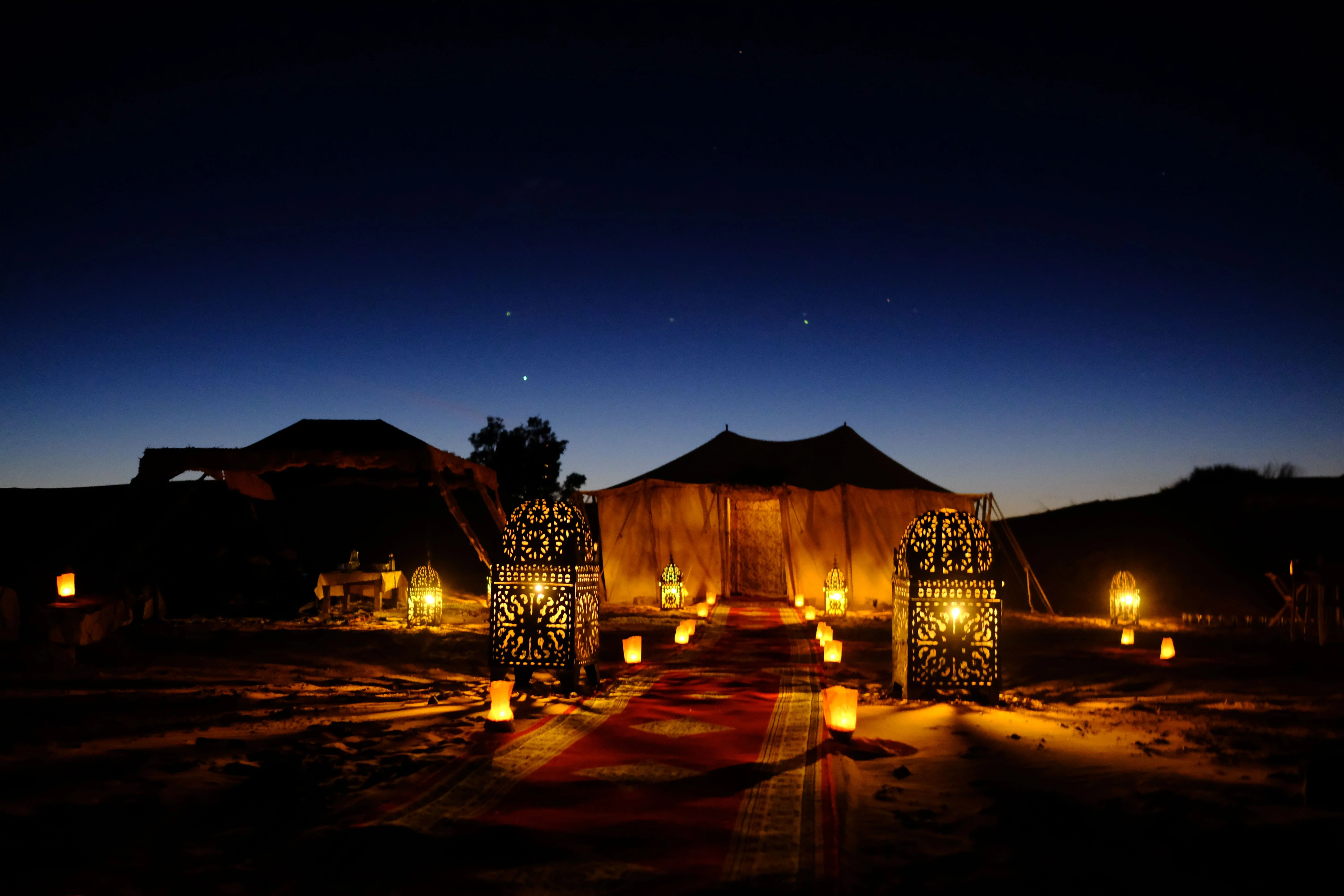 A private desert dinner tent illuminated by lanterns at dusk.