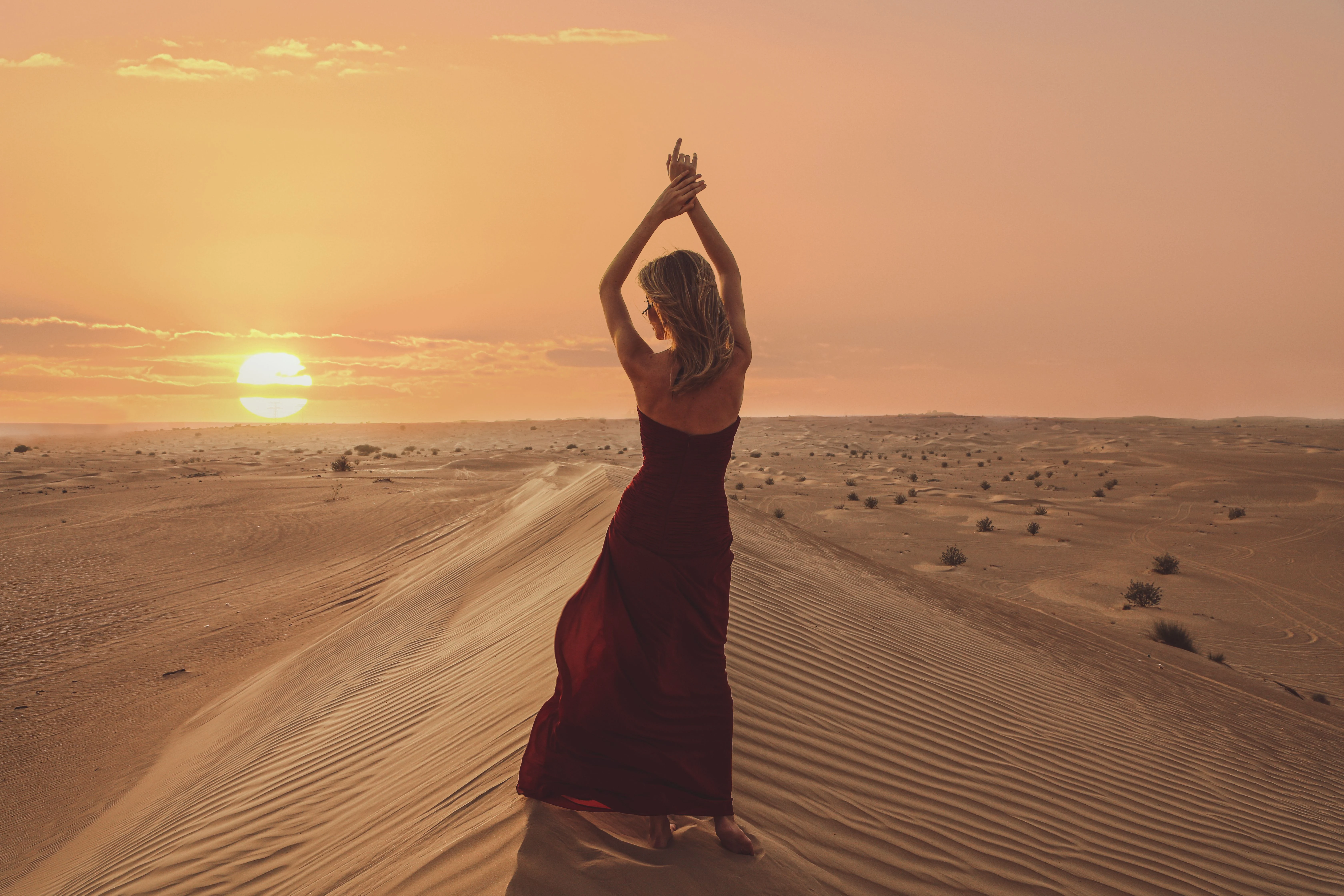 A woman standing on desert dunes at sunrise during a morning desert safari.