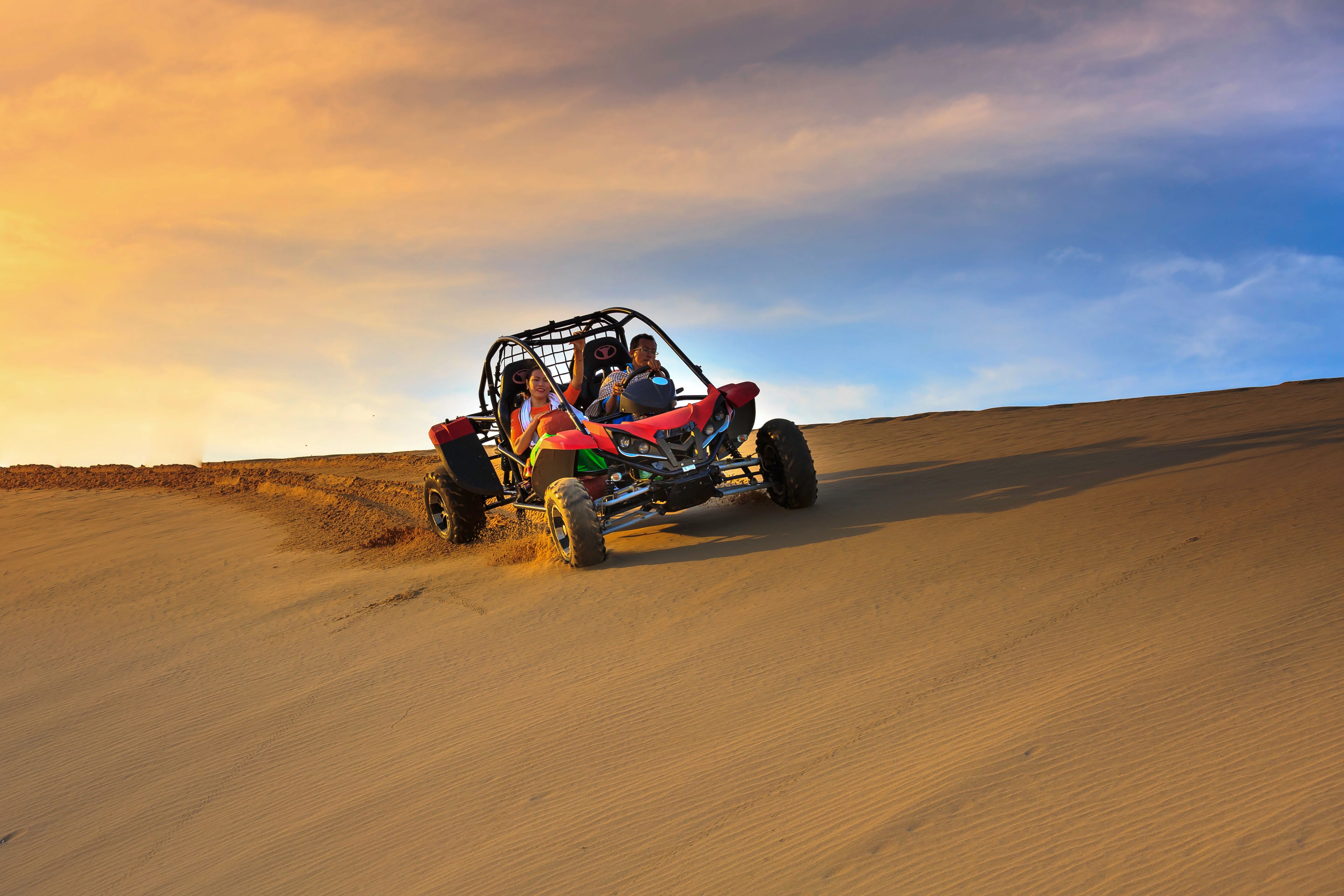Guests driving a red dune buggy across desert dunes at sunset.