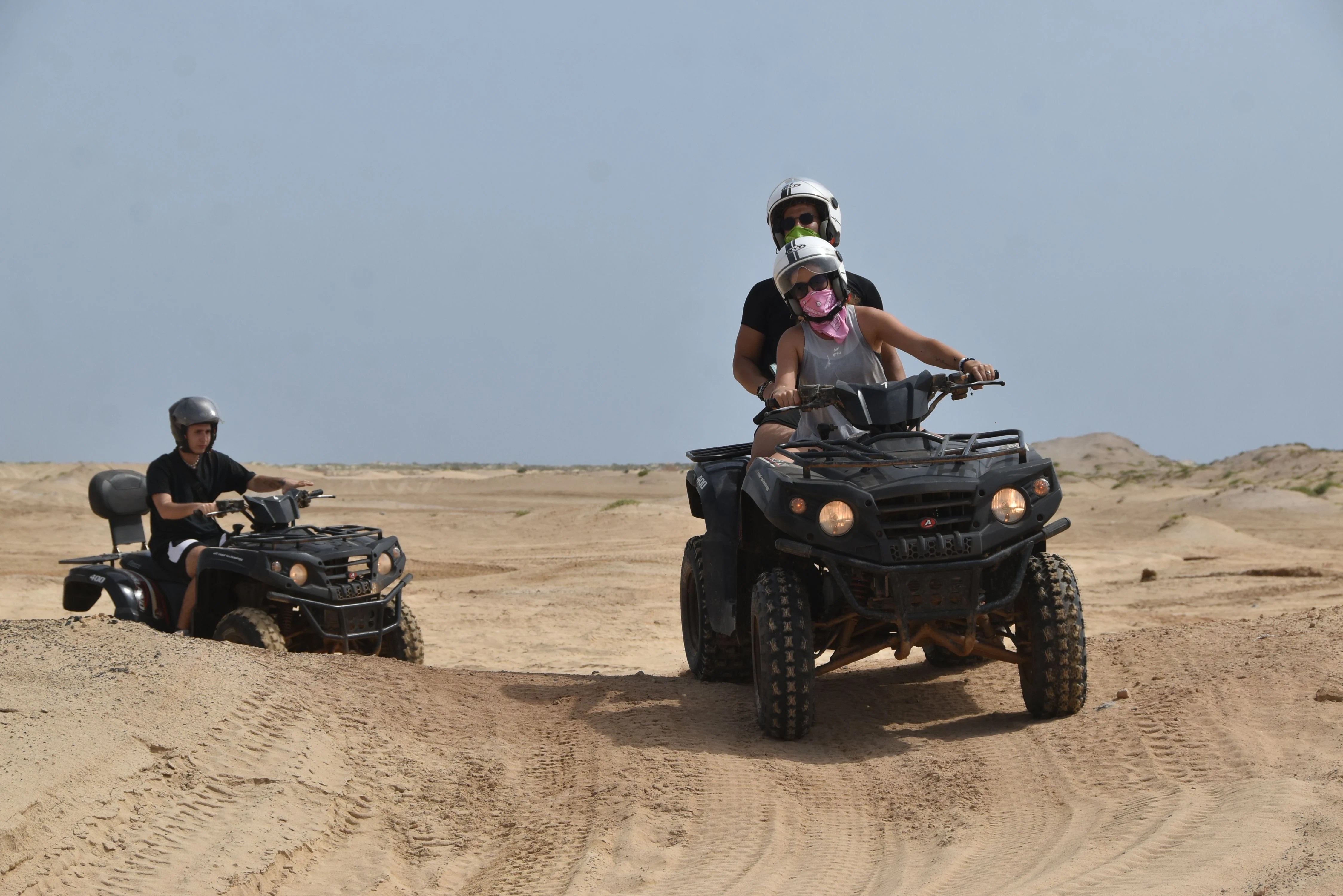 Guests riding quad bikes across a sandy desert track.