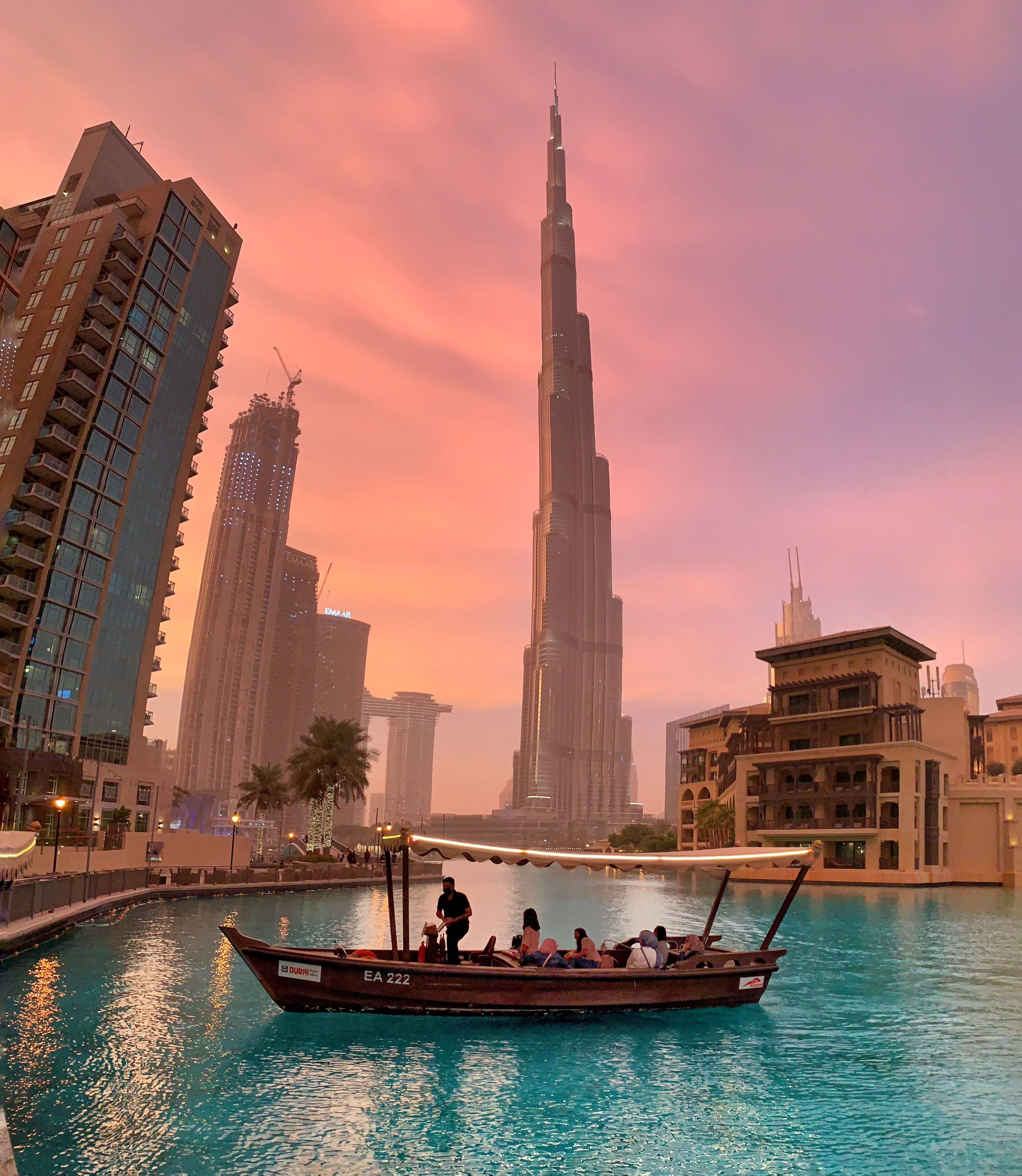 A traditional boat crossing Dubai water at sunset with Burj Khalifa in the background.