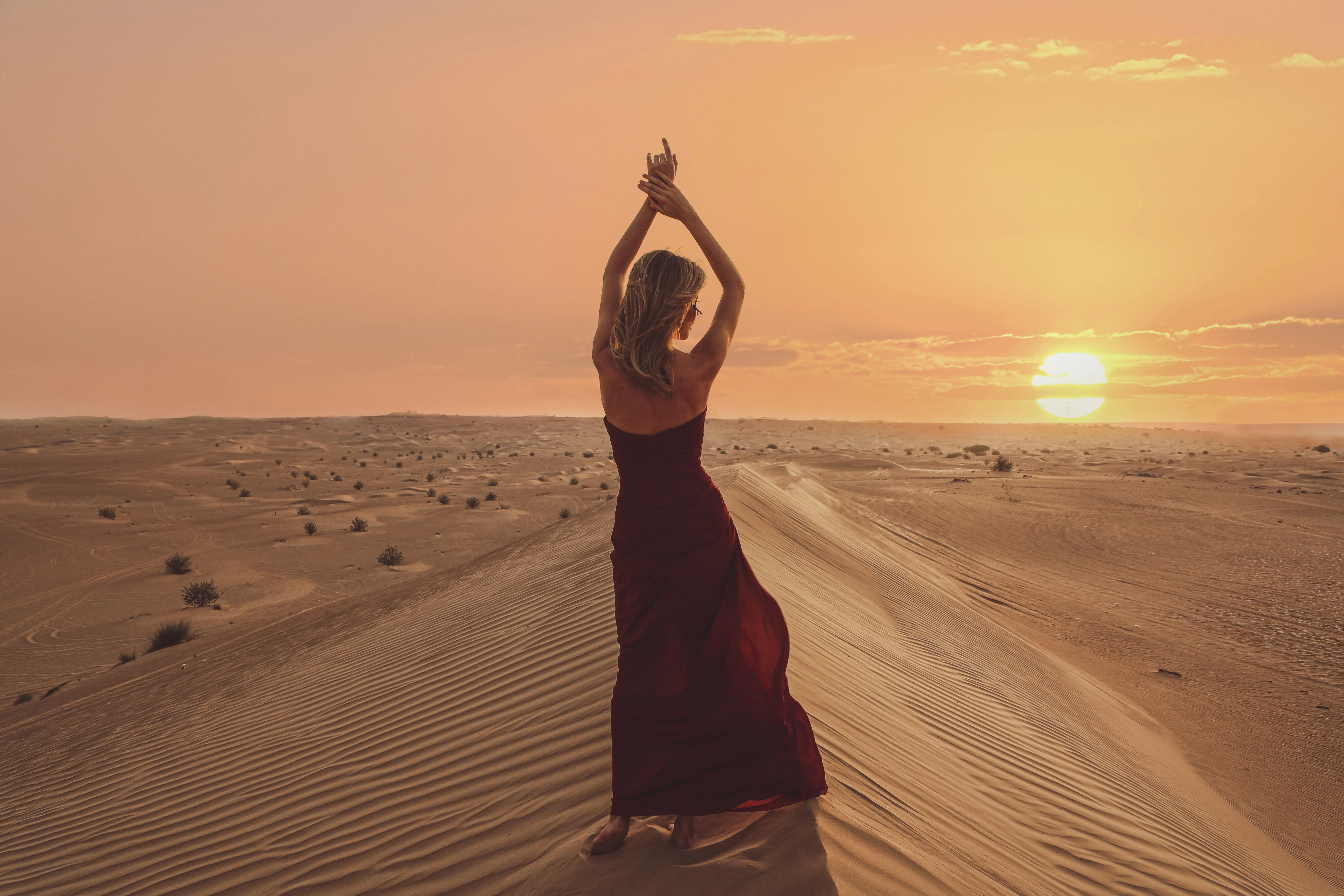 A woman standing on desert dunes at sunrise during a morning desert safari.