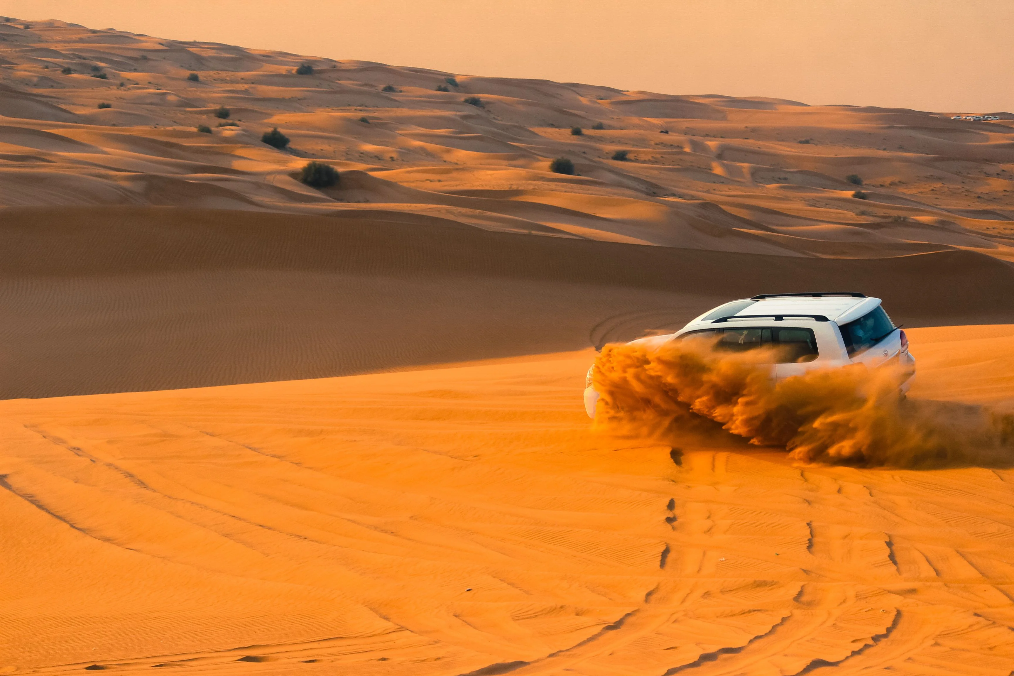 A 4x4 driving across golden desert dunes during an evening desert safari in Abu Dhabi.