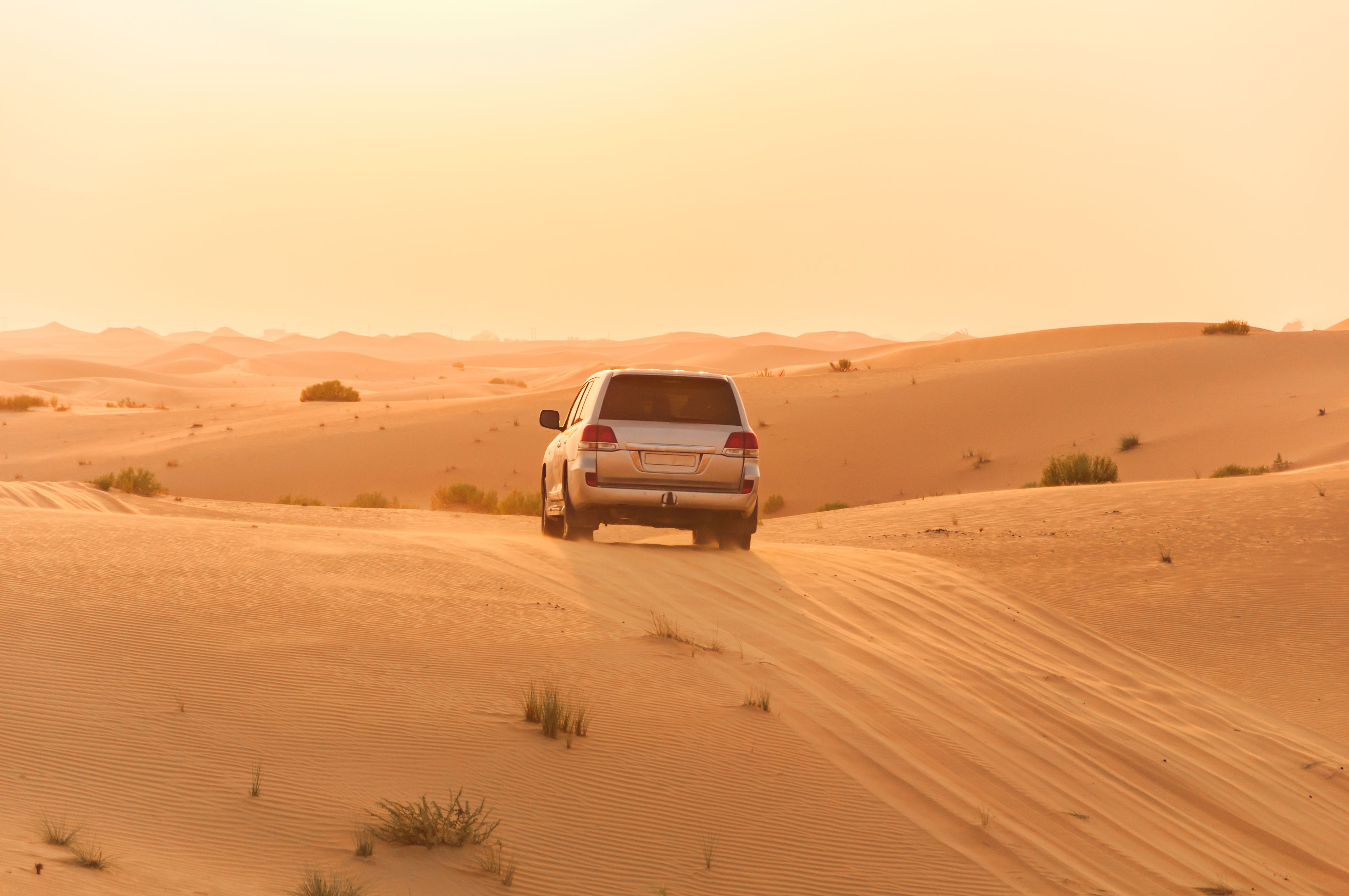 A vehicle crossing a wide golden desert landscape at sunset to represent scenic UAE escapes.